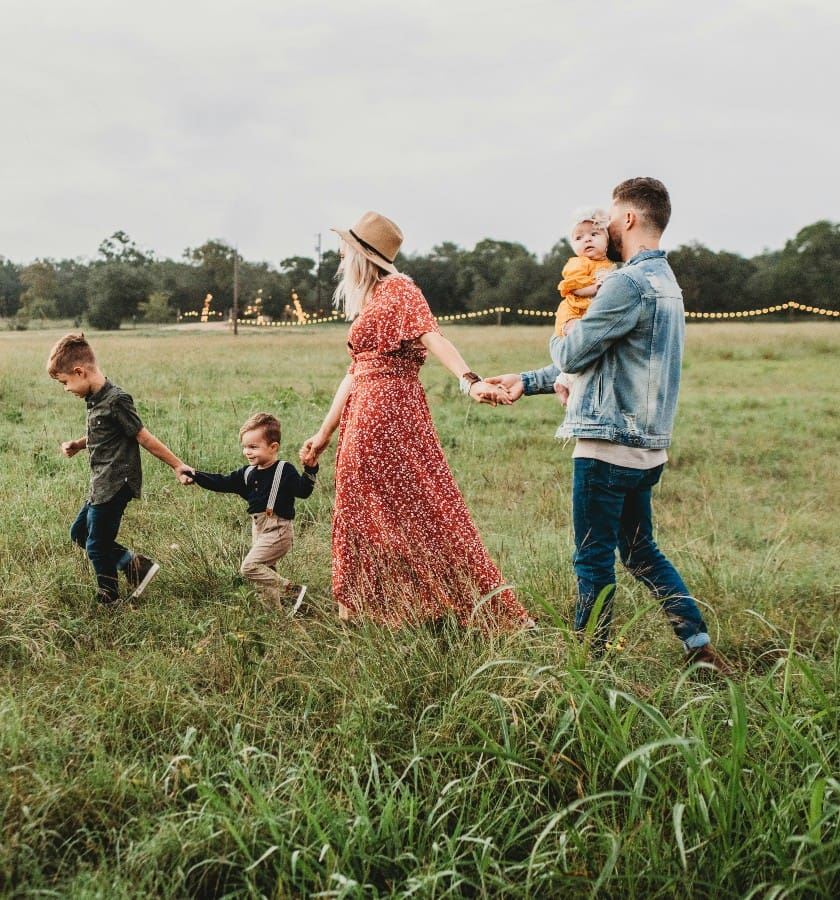 A family with three children, a mother and a father walk through a grass field.